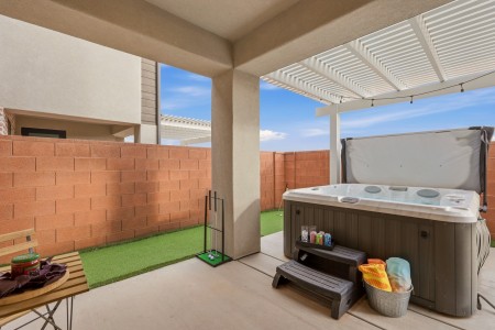 A backyard patio with a large hot tub under a covered area, red brick wall and outdoor seating nearby.