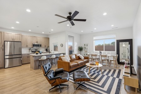 Open-concept living area with a brown leather sofa, black leather lounge chairs, and a striped rug facing a dining table by a large window.