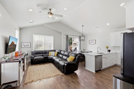 Open-concept living room and kitchen with a black leather sectional, white cabinets, and wood floors.